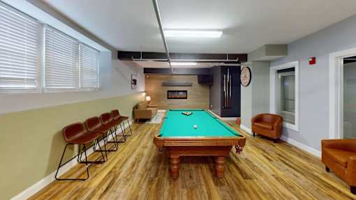 A pool table is surrounded by eight chairs in a room.