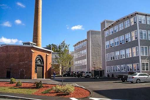 A brick building with a tall chimney is in front of a modern building.