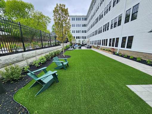 A white building with a black fence and green lawn chairs.