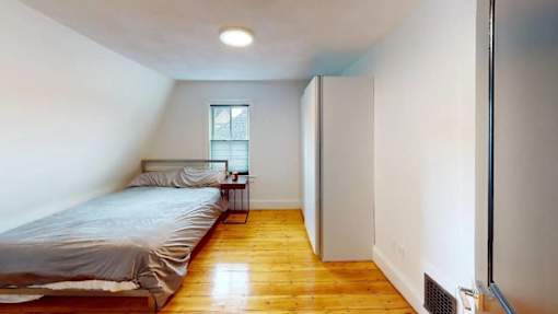 A bedroom with a bed, a nightstand, and a window.