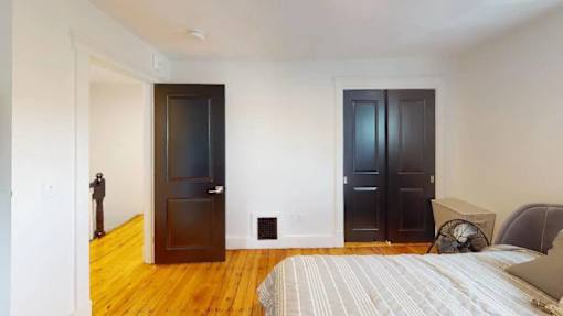 A bedroom with a bed, two doors, and a fan.