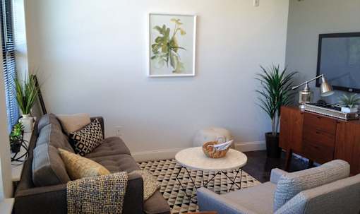 A living room with a brown couch, a white ottoman, and a painting on the wall.