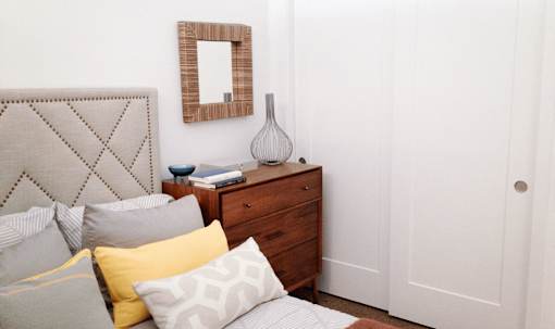 A bed with a grey headboard and pillows in front of a mirror and a dresser.