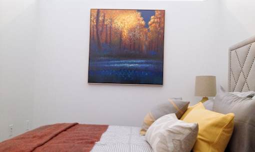 A bedroom with a bed, pillows and a painting on the wall.