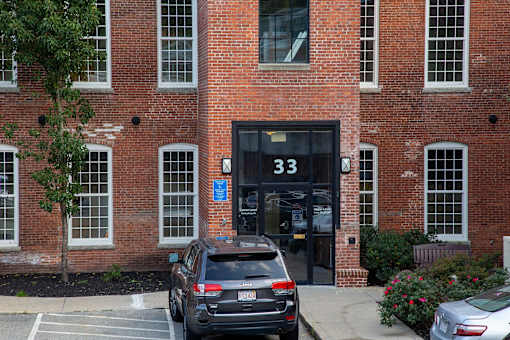 A black car is parked in front of a brick building with the number 33 on the door.