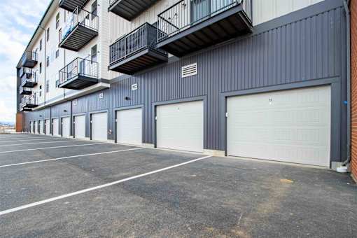 A parking lot in front of a grey building with black garage doors.