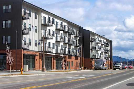 A modern apartment building with balconies and a parking lot in front.