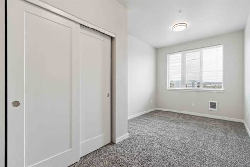 A room with a carpeted floor and a window with a view of buildings outside.