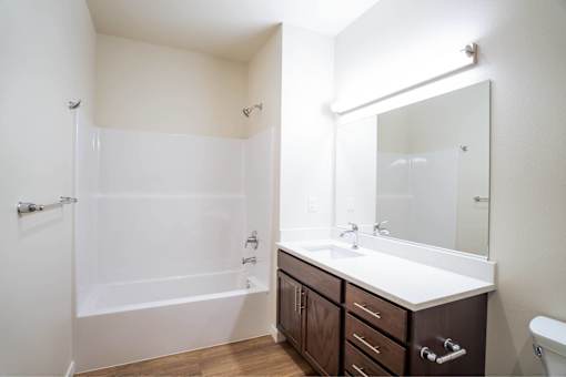 A white bathroom with a brown vanity and a white tub.