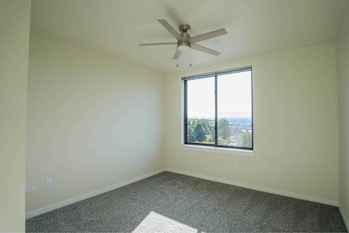 A room with a ceiling fan and a window overlooking a cityscape.