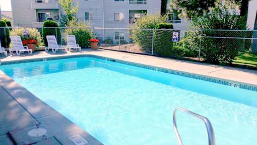 A swimming pool surrounded by a fence and chairs.