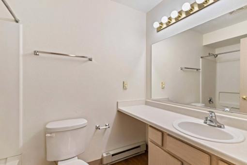 A white toilet is in a small bathroom with a sink and mirror.