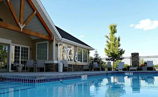 A pool in front of a house with a fence and a tree.