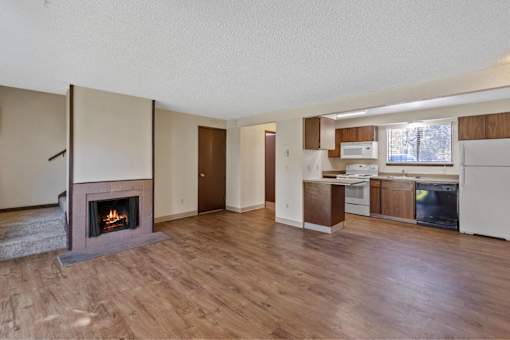 A living room with a fireplace and a kitchen area in the background.