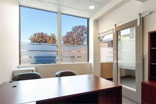 A conference room with a table, chairs, and a view of trees and buildings outside the window.