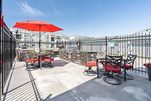 A patio with a red umbrella and chairs.