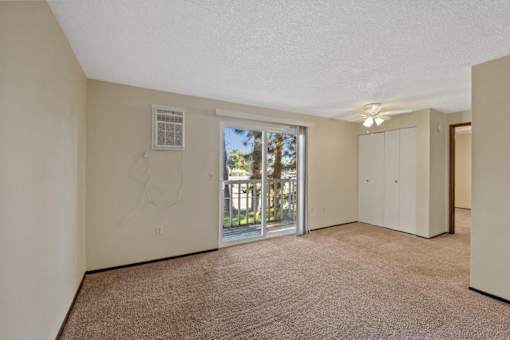 A room with a carpeted floor and a window with a view of trees and a building outside.