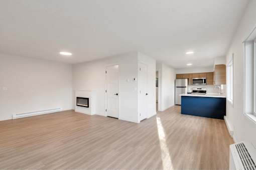 A spacious living room with a fireplace and a kitchen area in the background.