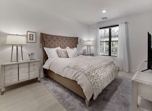 A bedroom with a large bed, a nightstand, and a window.