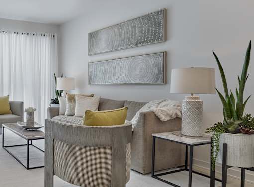 A living room with a grey couch, a glass table, and two framed artworks on the wall.