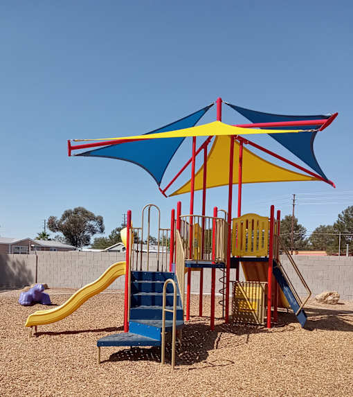 A playground with a blue and yellow umbrella and a yellow slide.