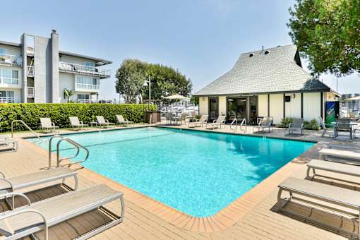 A large swimming pool surrounded by sun loungers and a building in the background.