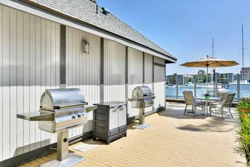 A patio with a grill and chairs overlooking a body of water.