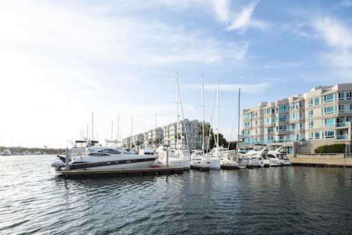 A yacht is docked at a marina with other boats and a building in the background.