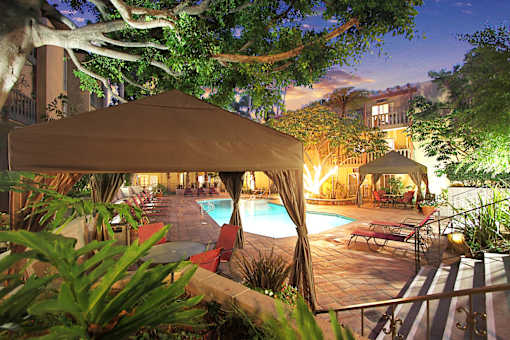 A poolside area with a tent and chairs is lit up at night.