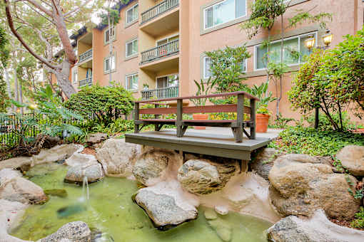 a bench sits on a bridge over a stream in front of an apartment building at Casa Granada, Los Angeles, CA