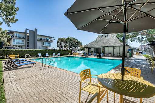 A sunny day at the pool with a yellow umbrella and chairs.