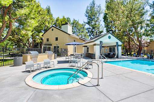 A pool with a hot tub and a house in the background.