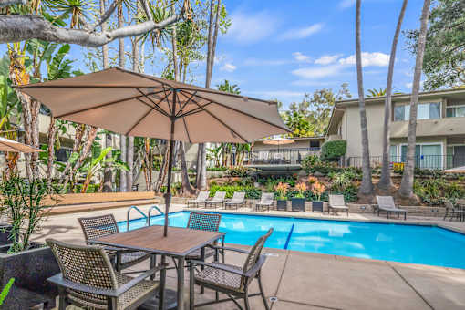 A patio with a table and chairs under an umbrella next to a pool.
