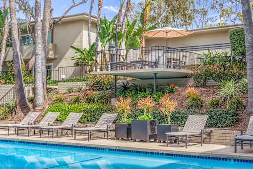 A pool surrounded by chairs and trees.