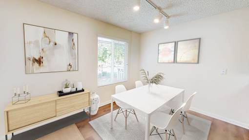 A white dining table with four chairs and a cabinet with a plant on top.