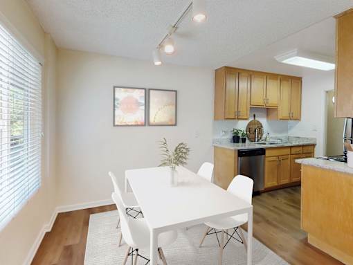 A white dining table with four chairs is in a kitchen with wooden cabinets.