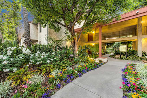 A garden with a concrete walkway and a building in the background at Village Pointe Apartments, Northridge, California