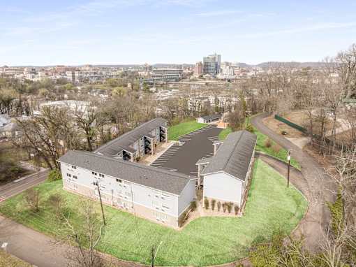 A large white building with a grey roof is surrounded by a green lawn.