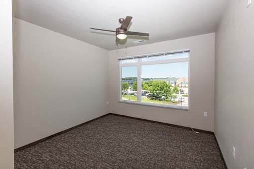 A room with a ceiling fan and a window overlooking a parking lot.