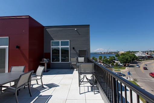 A balcony with a table and chairs overlooks a street and a mountain.