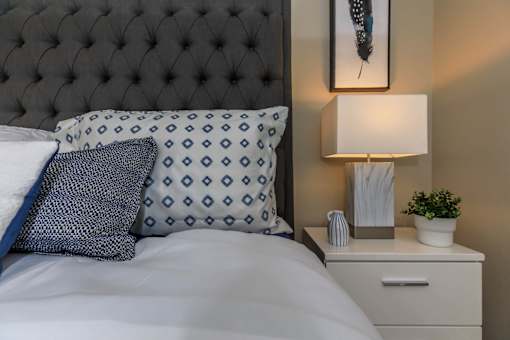 a bed with a blue and white pillow and a night stand with a lamp at Level 25 at The Curve by Picerne, Las Vegas, 89148