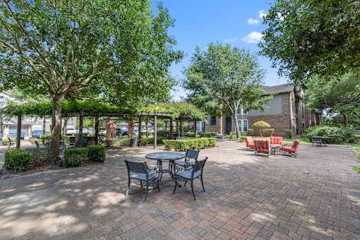 Large outdoor patio space with tables and chairs surrounded by trees at Asheville at Spring Branch apartments in Houston, TX
