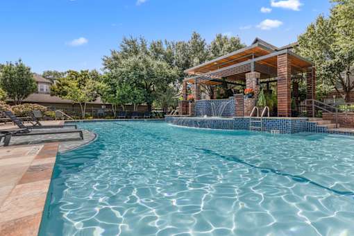 Pool with a fountain feature and pavilion in the background at Asheville at Spring Branch apartments in Houston, TX