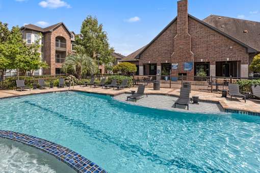 Resort style pool with in-pool loungers and the leasing office in the background at Asheville at Spring Branch apartments in Houston, TX