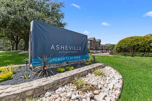 Property signage is displayed in front of a landscaped area at Asheville at Spring Branch apartments in Houston, TX