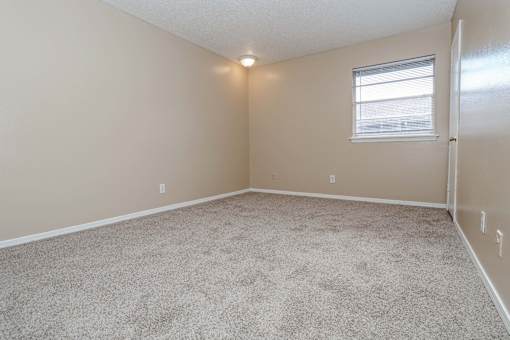 A bedroom with a carpeted floor and a window  at The Creole Apartments in Shreveport, LA