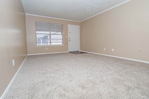 A living room with a carpeted floor and a window with blinds  at The Creole Apartments in Shreveport, LA