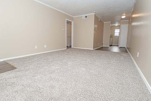A spacious carpeted living room that leads to the kitchen  at The Creole Apartments in Shreveport, LA