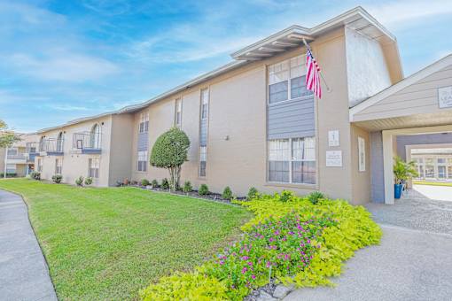 An apartment building with an American flag and a path leading to the leasing office at The Creole Apartments in Shreveport, LA