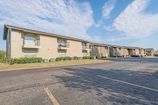A parking lot in front of an apartment building with a blue sky and clouds in the background at The Creole Apartments in Shreveport, LA